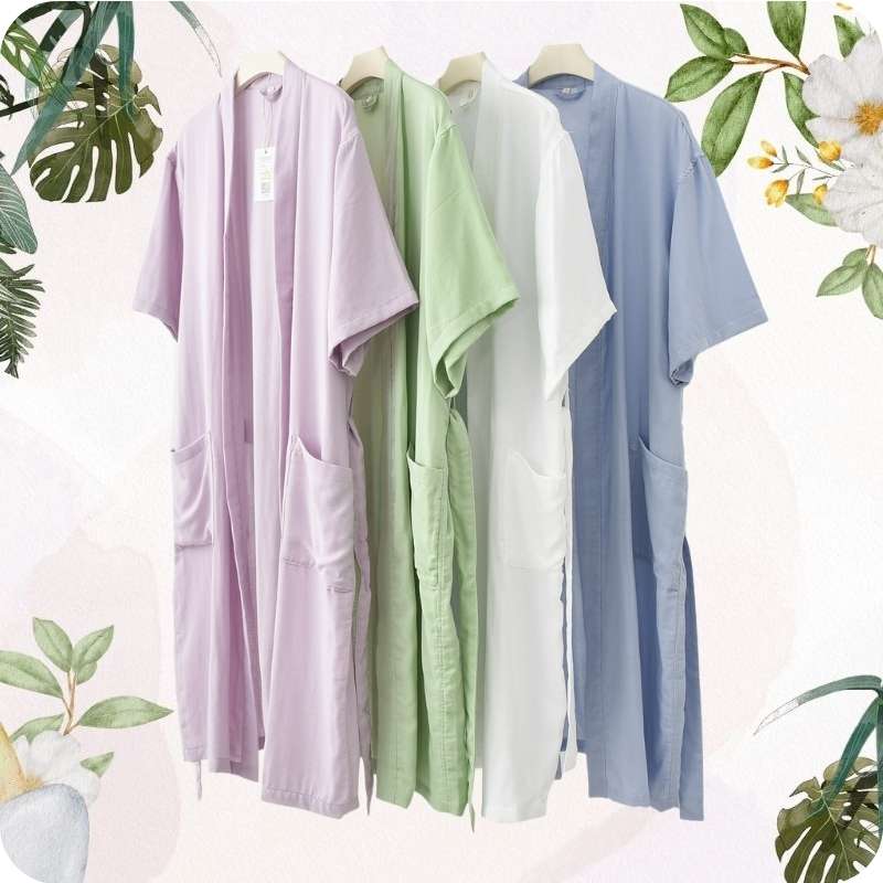 Four pastel-colored shirts on hangers with a soft white background and green leafy elements.