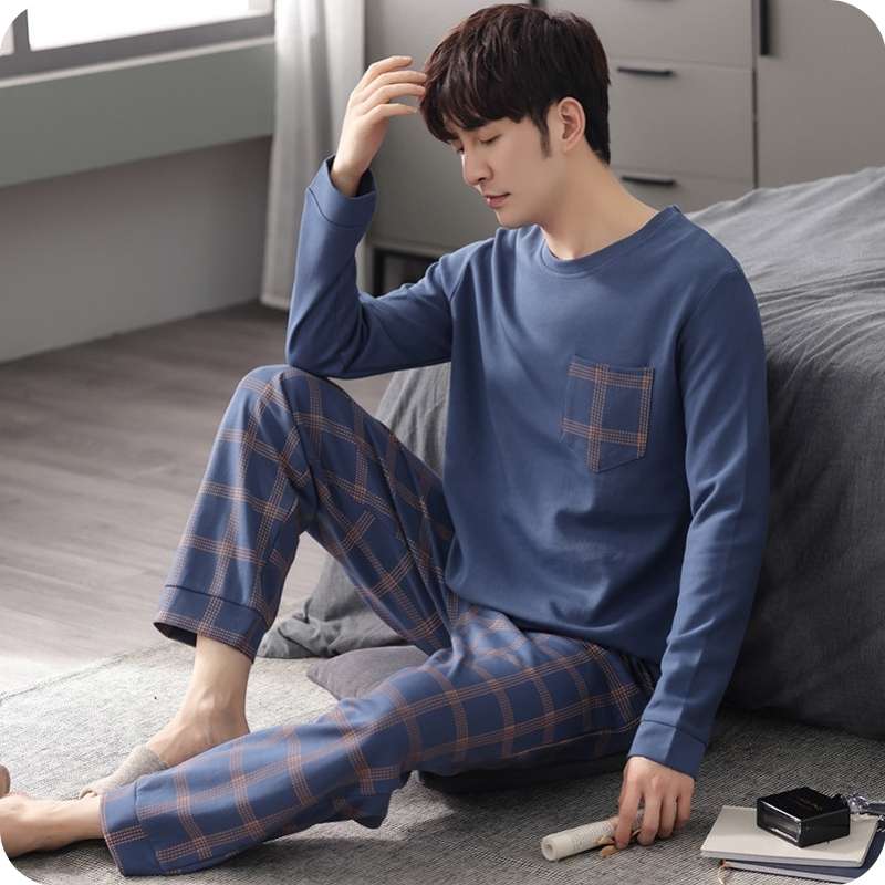 Man wearing blue pajama set sitting on a bed in a bedroom.
