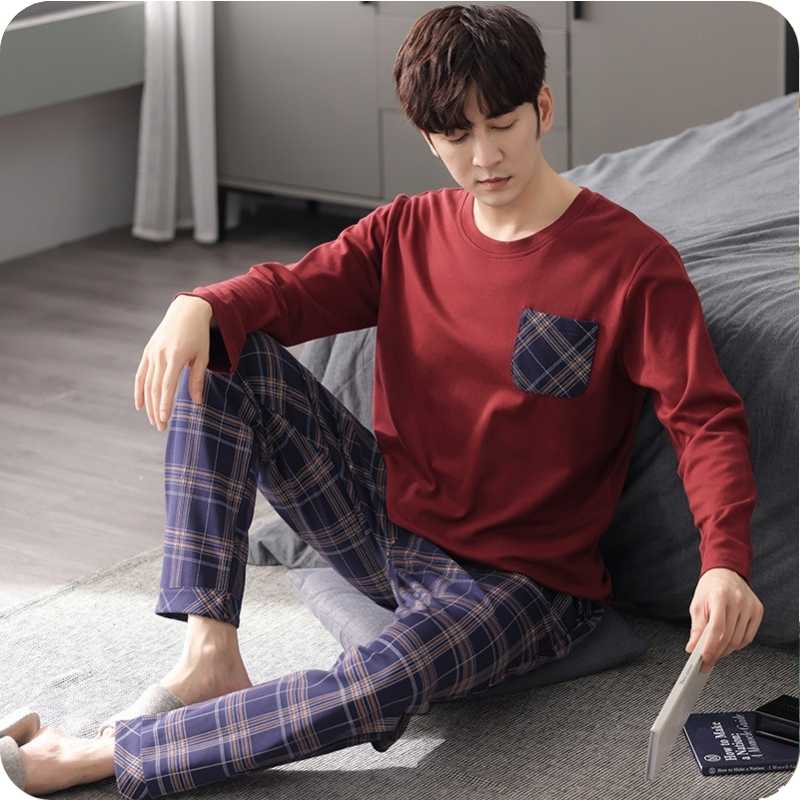 Person wearing a red long-sleeve shirt and plaid pants sitting on a bed.