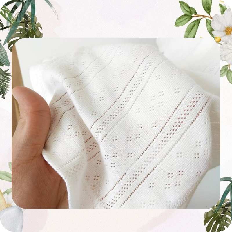 White textured fabric held by a hand with a floral and plant background