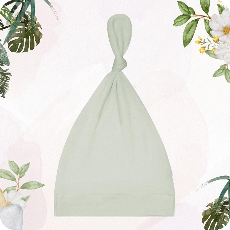 Green baby hat on a light pink background with floral and plant decorations