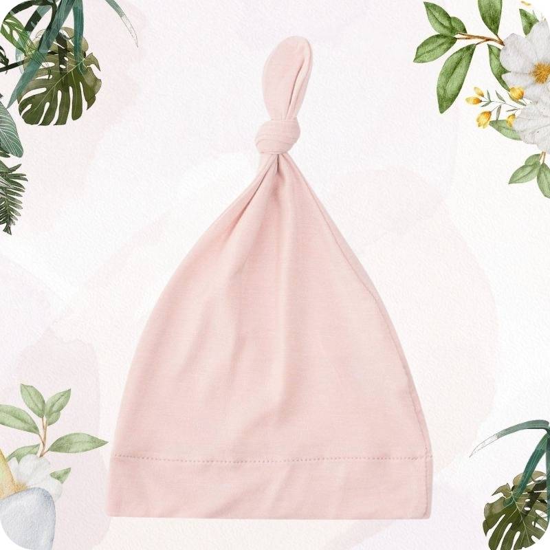 Pink baby hat on a light pink background with green leaves and flowers.