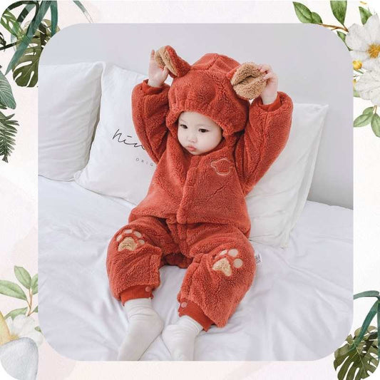 Baby in a brown fleece outfit with animal ears sitting on a white cushion.