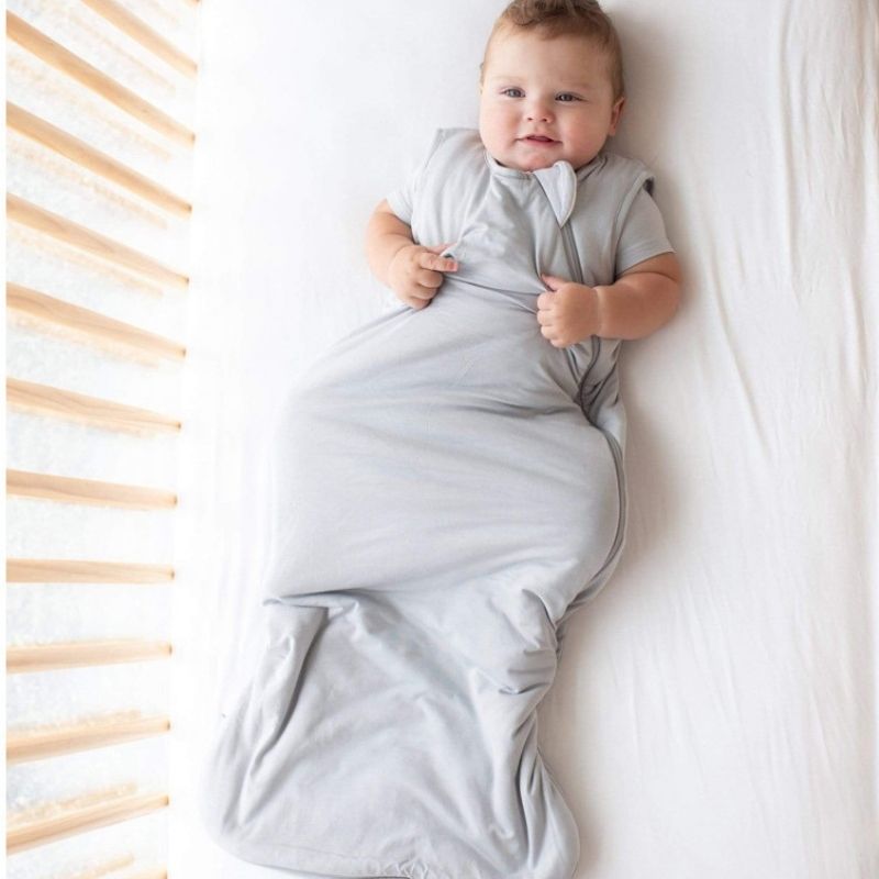 Baby wrapped in a gray swaddle on a white blanket with wooden bars in the background