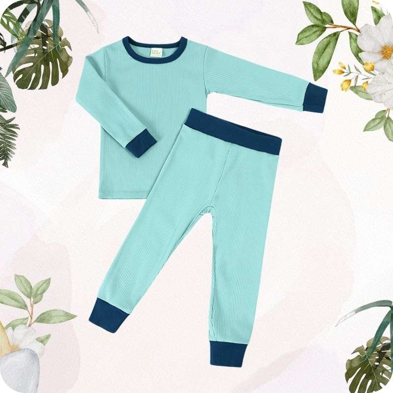 Children's teal pajama set with navy cuffs on a light pink background with floral elements.