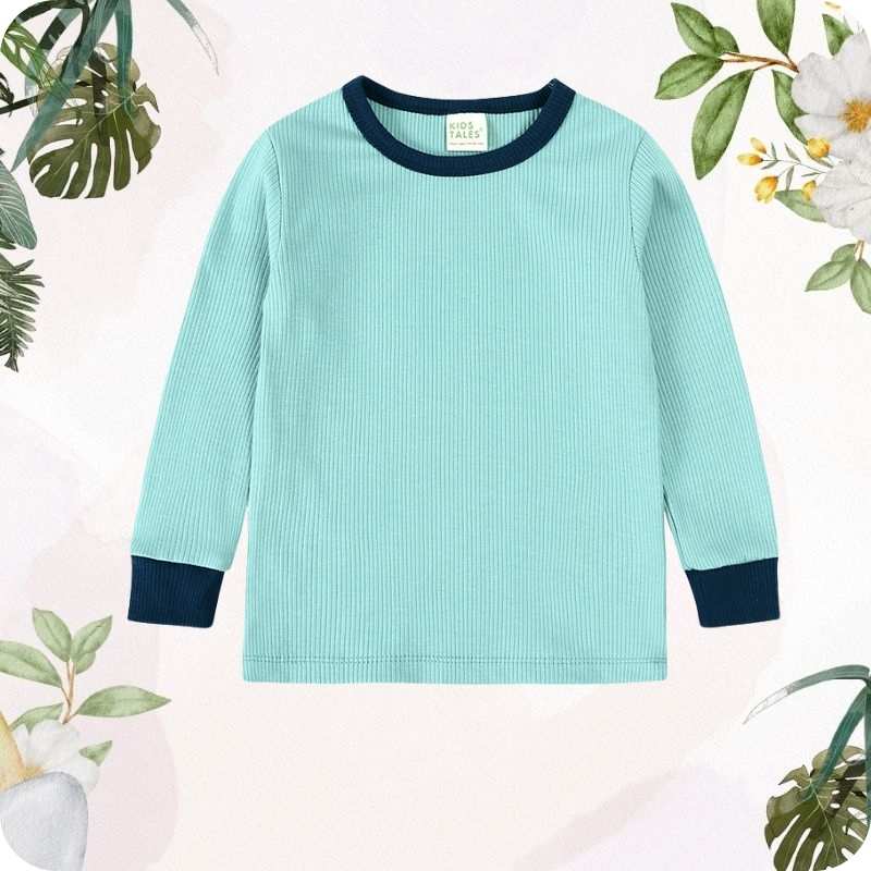 Light blue sweater with dark blue cuffs and hem on a light pink background with greenery.