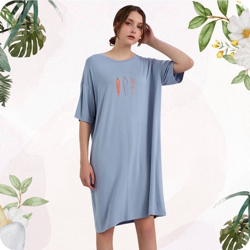 Woman wearing a blue nightshirt with vegetable design on a light background with green foliage.