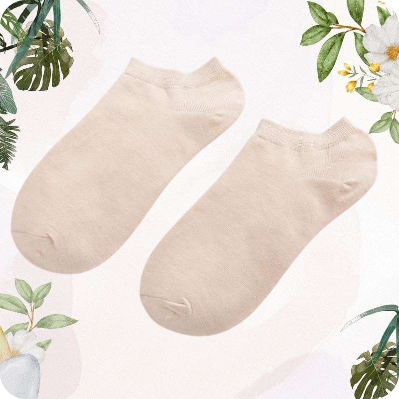 Pair of skin color ankle socks on a light pink background with green leaves and flowers.