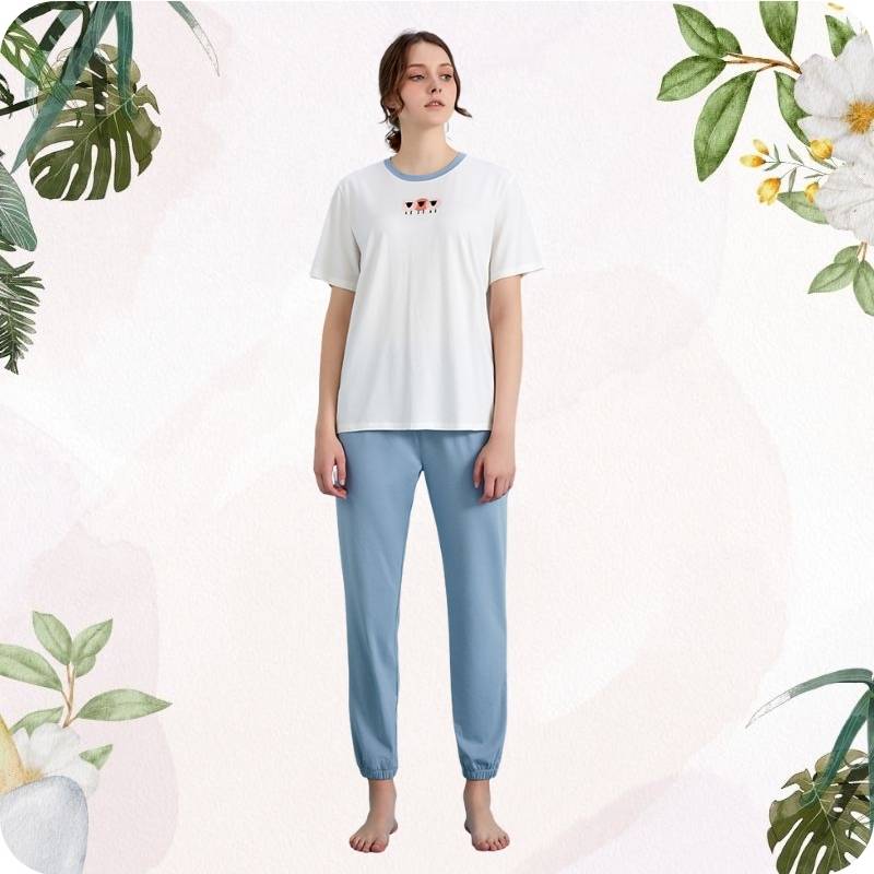 Woman wearing a white t-shirt and light blue pants with floral and leaf decorations on a light pink background