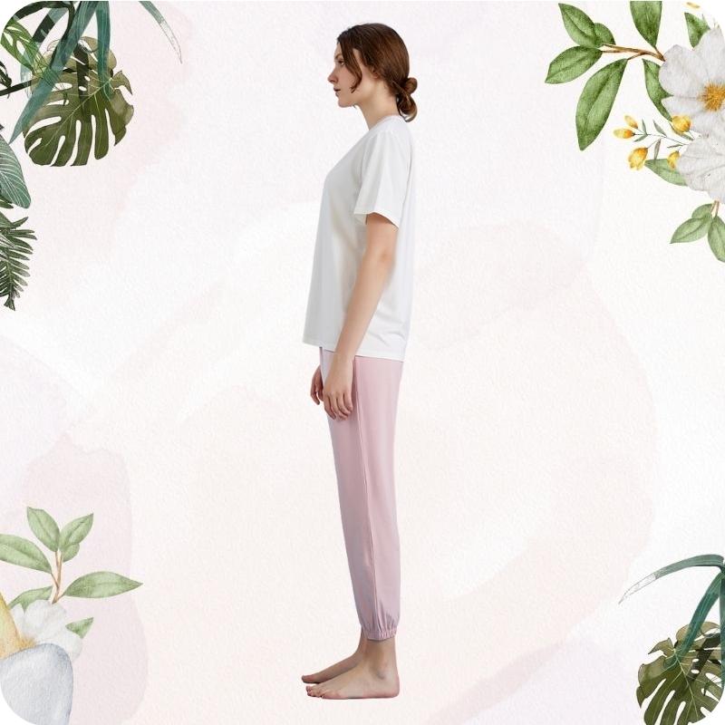 Woman wearing a white top and pink pants with floral and leaf decorations on a light background