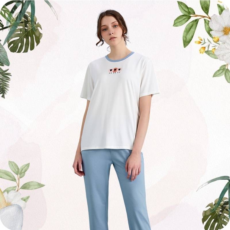 Woman wearing a white t-shirt with a logo and light blue pants on a light background with floral elements.