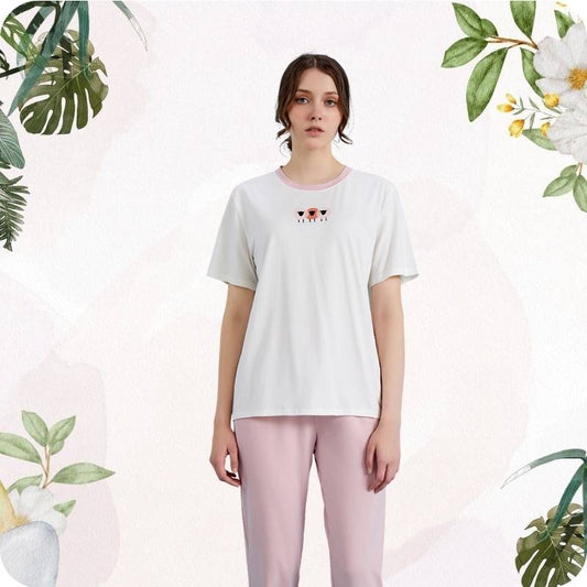 Woman wearing a white t-shirt with a design and pink pants against a light background with green foliage.