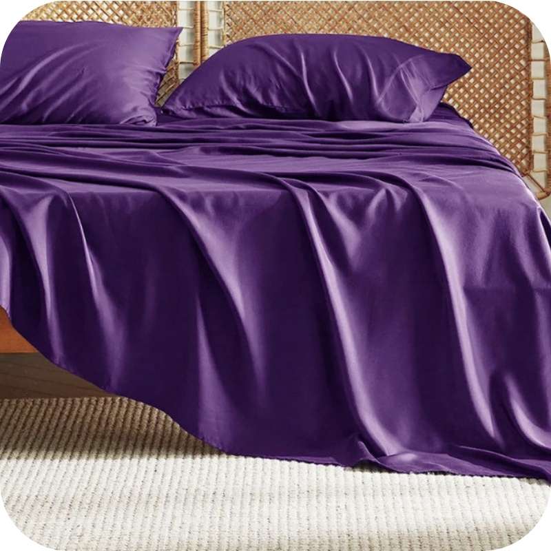 A dark purple bamboo fiber bed sheet set on a bed, including a fitted sheet, pillowcase, and two additional pillowcases.