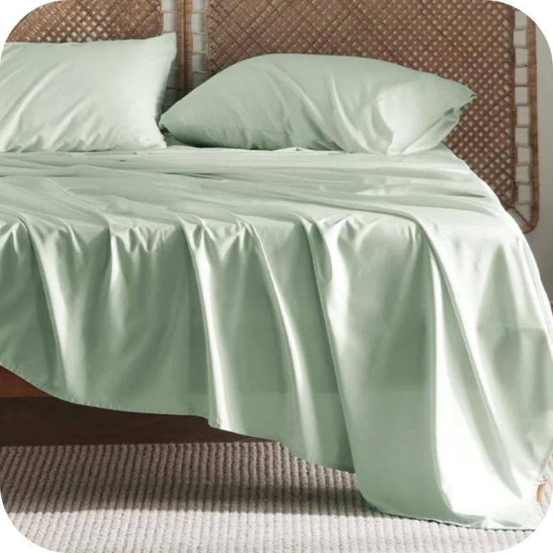 A light green bamboo fiber bed sheet set on a bed, including a fitted sheet, pillowcase, and two additional pillowcases.