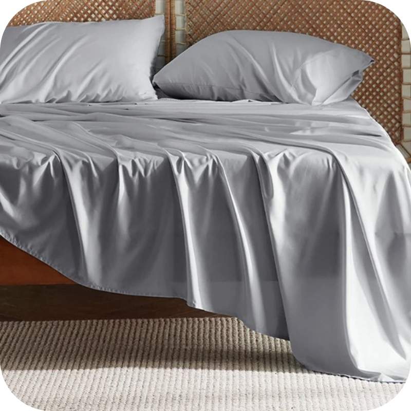 A light grey bamboo fiber bed sheet set on a bed, including a fitted sheet, pillowcase, and two additional pillowcases.