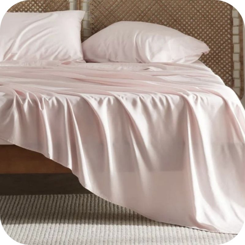 A light pink bamboo fiber bed sheet set on a bed, including a fitted sheet, pillowcase, and two additional pillowcases.