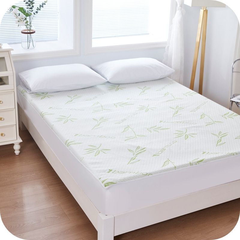 A white mattress protector cover with a bamboo fiber air layer and a floral pattern, placed on a bed in a room with a window and a nightstand.